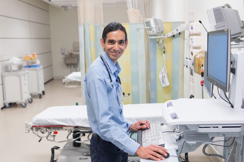 Kris Srinivasan wearing a button down shirt and working at a computer station.